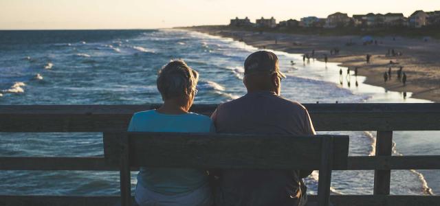 Married couple a bench staring at ocean.